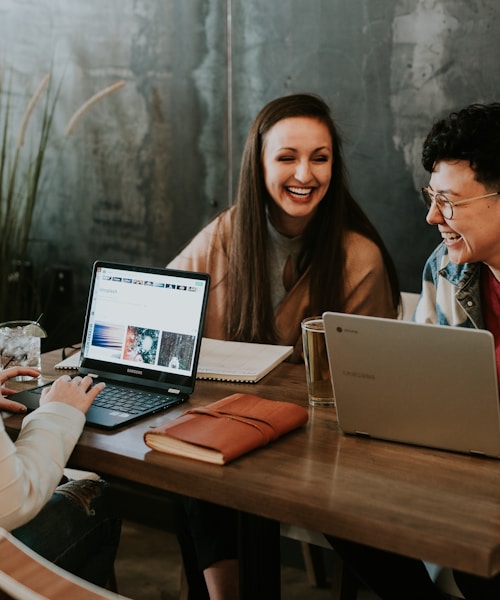 Two women laughing together during a working session with laptops at a shared table